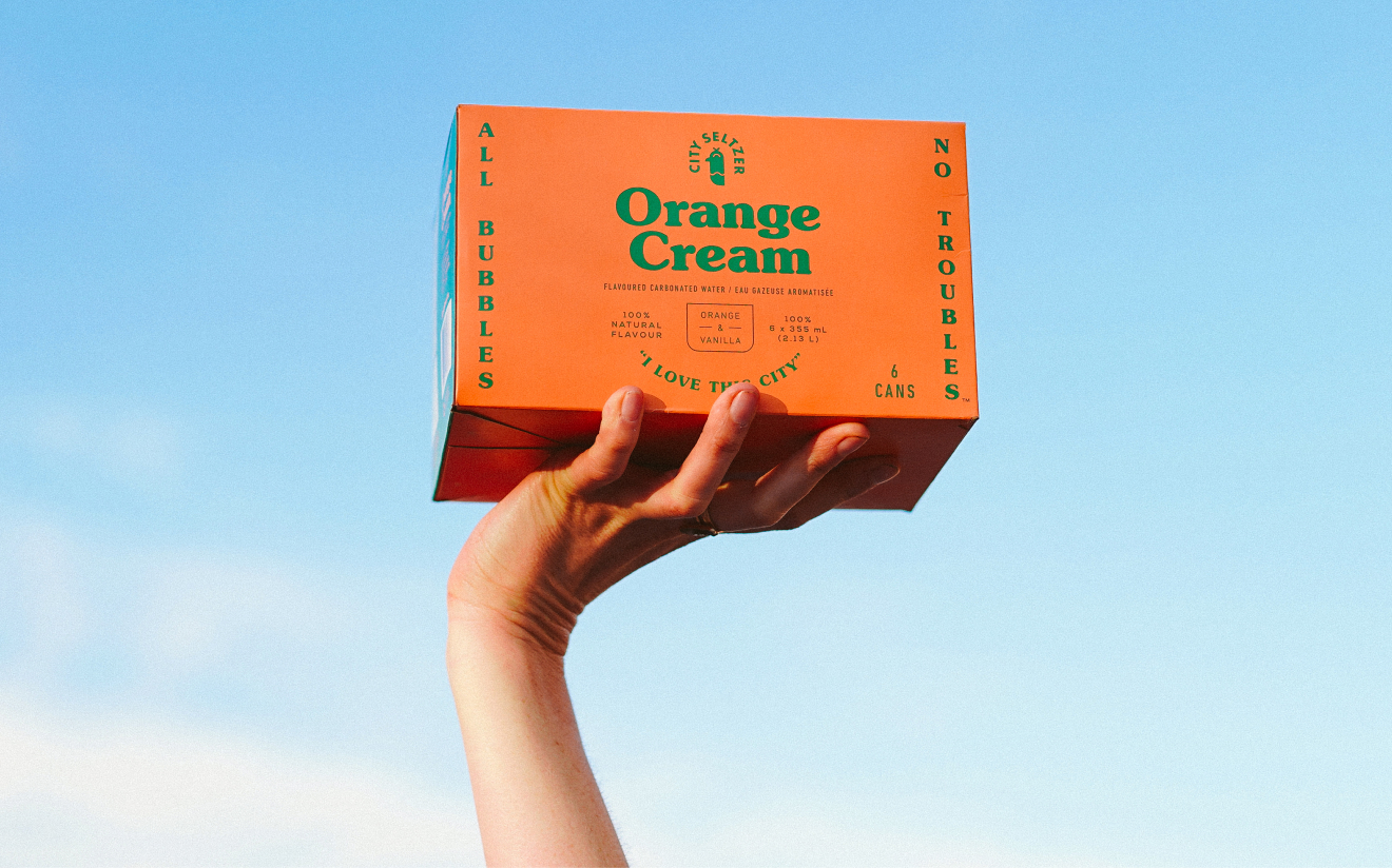 Hand holding aloft a beautiful case of Orange Cream flavoured City Seltzer.